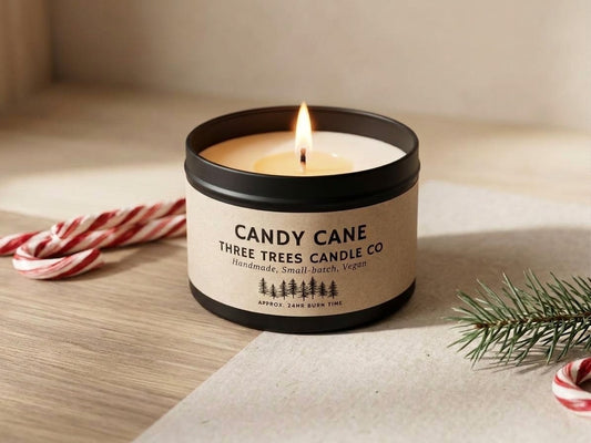 Lit Candy Cane scented tin candle glowing on a cozy wooden surface