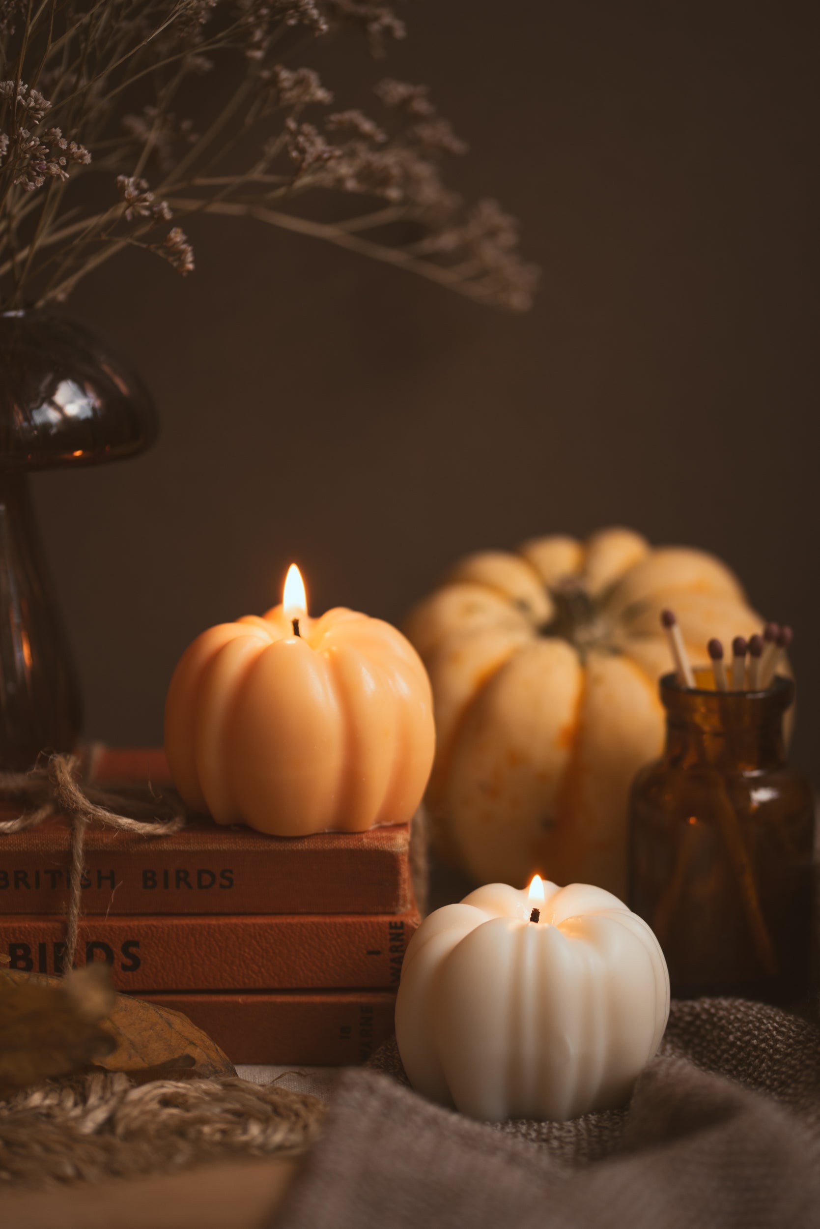 Pumpkin candle styled on fall-themed table with leaves and books